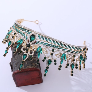 Detailed macro view of vintage gold crown featuring emerald green gems on a wooden chest