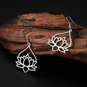 Silver lotus drop earrings hanging on dark wood with intricate hollow-out floral details