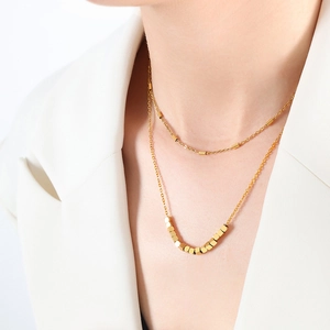 Collier double couche doré élégant avec cubes géométriques et perles sur un modèle