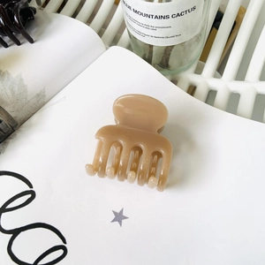 Beige matte claw clip hair accessory placed on a minimalist white open notebook