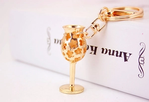 Close-up of golden metal wine glass keychain with hollow flower pattern on a white book