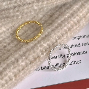 Close-up of gold and silver twisted knot rings on a beige knitted background