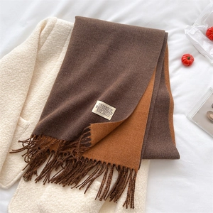 Detailed macro view of dual-color brown and camel scarf with fringes and brand label