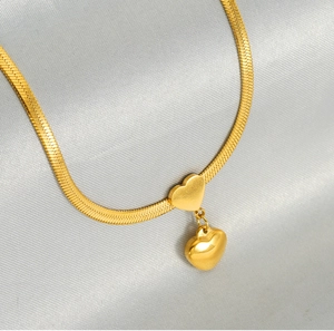 Macro detail of gold double heart pendant on a flat snake bone chain with satin texture