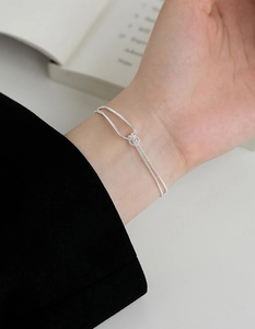 Detail of a minimalist silver knot bracelet featuring a sleek arc and fine grain chain