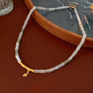 Detailed close-up of bamboo leaf necklace with jade beads and gold pendants on tray