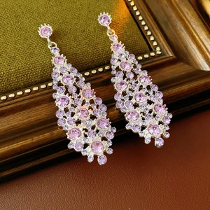 Vista macro de pendientes largos con diamantes rosa sobre un marco de fotos retro