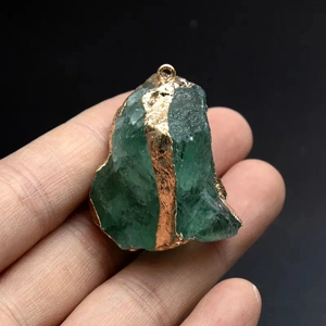 Macro detail of raw green fluorite pendant with gold electroplated edges on black background