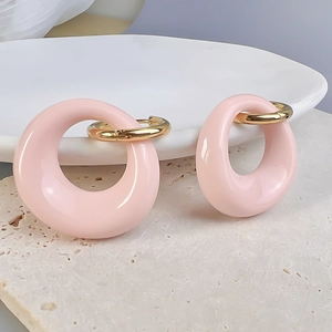 Close-up of pink oval enamel pendant earrings with gold hoops on white porcelain plate