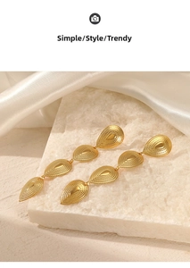 Detail view of gold drop earrings with textured pattern on white stone and silk surface