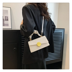 Détail du sac blanc en cuir avec fermoir doré et anse froncée sur un blazer noir chic