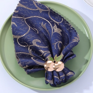 Detailed view of a golden cherry napkin ring with green leaves on a blue patterned napkin