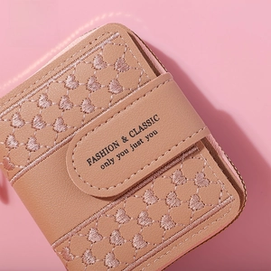 Detail of pink faux leather wallet featuring heart embroidery and magnetic buckle