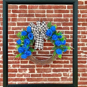 Close-up of blue rose Christmas wreath with black and white plaid bow on a red brick wall