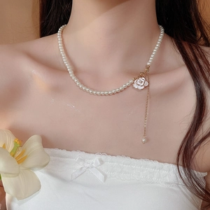 Detailed close-up of a white camellia pearl necklace with gold tassel on a model