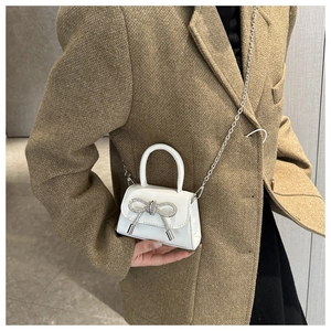 Detail of white mini patent leather bag with rhinestone bow and silver chain strap