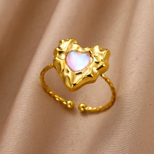 Close-up of heart-shaped iridescent stone ring with gold twisted rope band and silk background