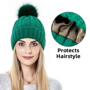 Dettaglio berretto in maglia verde smeraldo con fodera in raso e pompon decorativo