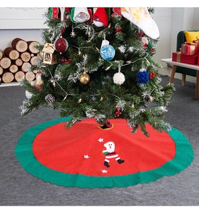 Detailed view of red Christmas tree skirt with wavy green edges and Santa Claus pattern