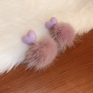 Close-up of stylish purple heart earrings with soft pom-pom fur balls on a fuzzy surface