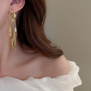 Detail of long golden tassel earrings with leaf elements on female model for style