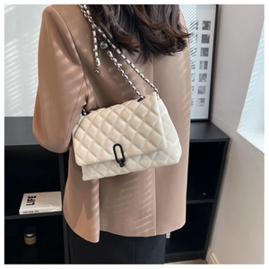 Detail of cream quilted chain bag worn by model featuring elegant metal lock and texture