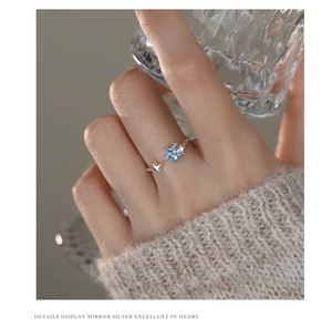 Detail shot of a s925 silver star ring with blue zircon worn by a model holding a glass