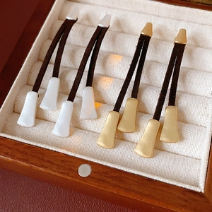 Detail view of gold and silver tassel earrings with leather cords in a jewelry box