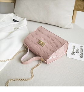 Détail du sac à main rose gaufré crocodile avec fermoir doré posé sur un canapé