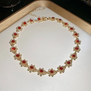 Macro detail of a gold necklace with red floral gems on a white tray with gold edges