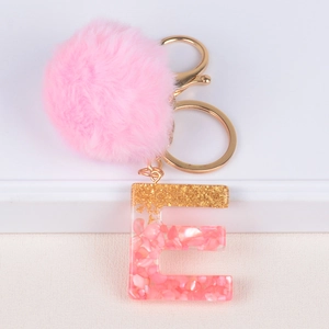Detailed macro view of pink resin letter E keychain with fluffy faux fur pompom and gold foil