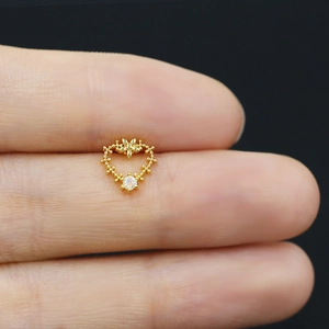 Macro shot of a tiny gold heart-shaped nose stud with opal stone on a finger tip