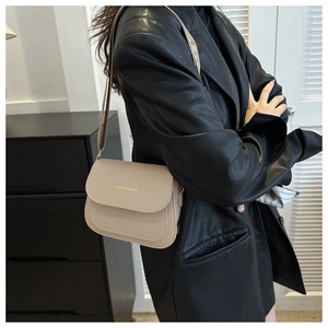 Detail of beige crocodile pattern saddle bag with gold logo worn by model in black leather jacket