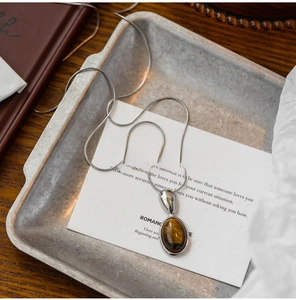 Detail of tiger eye stone pendant on sleek silver snake chain with metallic plate