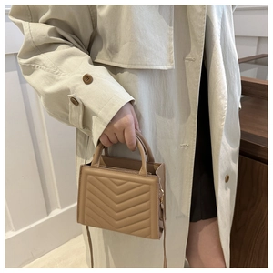Detail of khaki chevron quilted handbag featuring dual handles and long shoulder strap