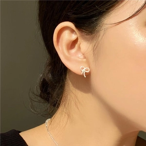 Close-up of a sparkling silver bow stud earring with diamonds on a model's ear