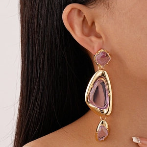 Close-up of oversized gold-tone earrings with purple acrylic stones on a model