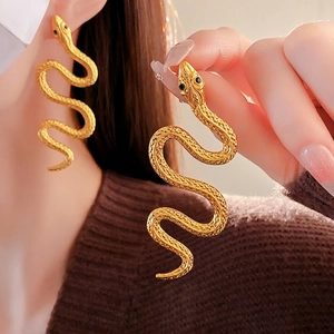 Exaggerated golden snake stud earrings with green gemstone eyes and scaly metal texture