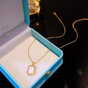 Detail of a gold titanium necklace with a white rectangle pendant and zircon in a blue box