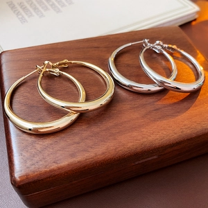 Classic gold and silver hoop earrings displayed on a rustic wooden stand with a soft background