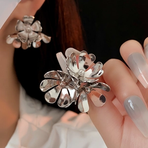 Close-up of oversized silver floral earrings with a metallic finish on a model