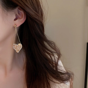 Close-up of golden tassel earrings featuring a sparkling champagne heart-shaped pendant