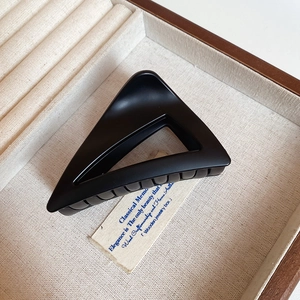 Close-up of matte black triangle hair claw clip on linen fabric inside a jewelry box