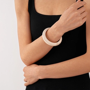 Macro detail of cream acrylic geometric open bangle with vertical grooved texture