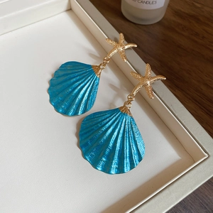 Macro shot of gold starfish and blue shell earrings in a beige jewelry box with a candle