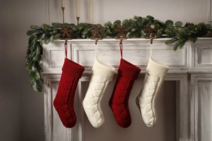 Close-up of four red and white cable knit Christmas stockings hanging on a white fireplace