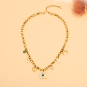 Macro shot of gold charm necklace featuring heart, moon, and green gemstone pendants