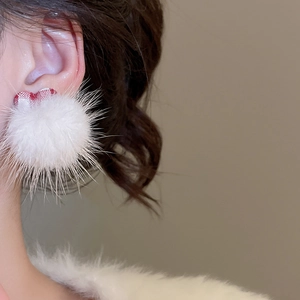 Close-up of white plush pom-pom earring with red and white plaid fabric detail