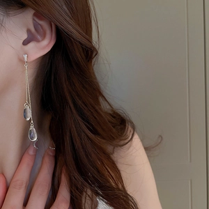 Detailed view of long gold tassel earrings with clear teardrop pendants and zircons