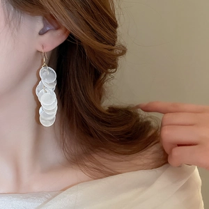 Detail of long cascading earrings with translucent white shell-like discs and gold hooks